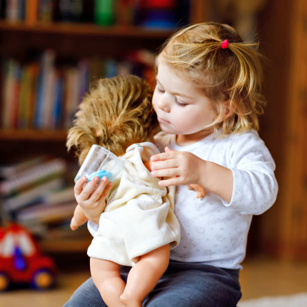 人形で遊ぶ愛らしいかわいい幼児の女の子。幸せな健康な赤ちゃんの子供は、自宅や保育園で母親を再生し、ロールゲームで楽しんで幸せ。おもちゃを持つアクティブな娘 - baby doll dress ストックフォトと画像