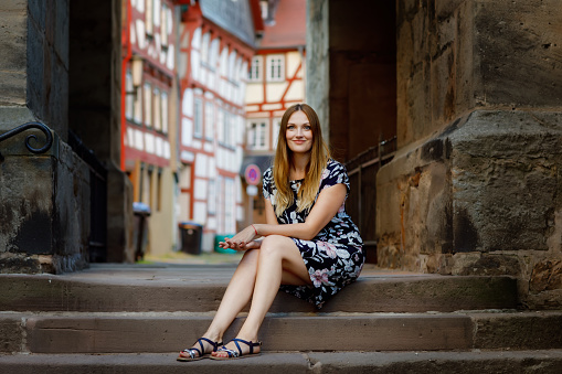 Beautiful young woman with long hairs in summer dress going for a walk in German city. Happy girl enjoying walking in cute small fachwerk town with old houses in Germany