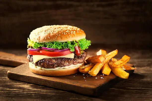 Delicious Hamburger with cheese and french fries on wooden table and dark background