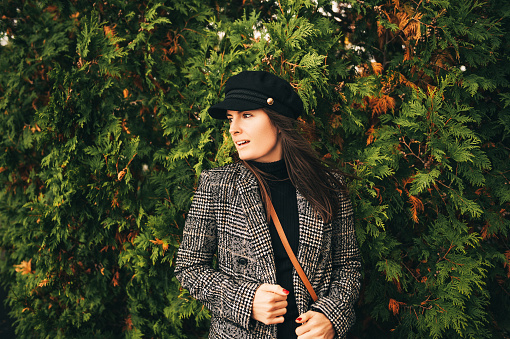 Outdoor portrait of beautiful young woman with dark hair, wearing check blazer and black cap