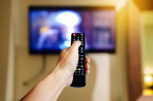 Hand holding television and audio multimedia remote control for watching tv
