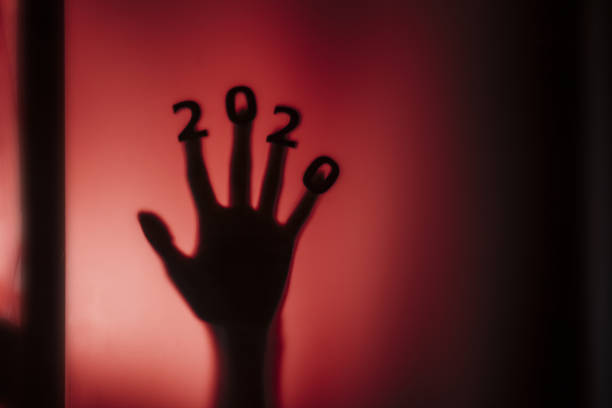 silhouette of a female hand with date on fingers pressed to glass of door with a red strange backlight, destruction of the stereotype happy new year, entering 2020 horror genre silhouette of a female hand with date on fingers pressed to glass of door with a red strange backlight, destruction of the stereotype happy new year, entering 2020 horror genre thriller film genre stock pictures, royalty-free photos & images