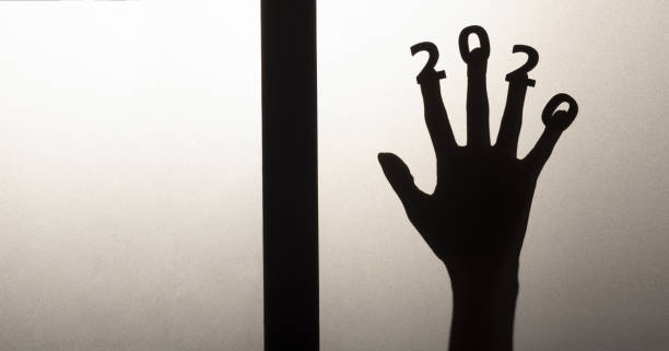 silhouette of a female hand with date on fingers pressed to glass of door, destruction of the stereotype happy new year, entering 2020 horror genre silhouette of a female hand with date on fingers pressed to glass of door, destruction of the stereotype happy new year, entering 2020 horror genre thriller film genre stock pictures, royalty-free photos & images