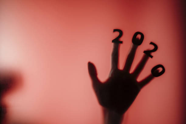silhouette of a female hand with date on fingers pressed to glass of door with a red strange backlight, destruction of the stereotype happy new year, entering 2020 horror genre silhouette of a female hand with date on fingers pressed to glass of door with a red strange backlight, destruction of the stereotype happy new year, entering 2020 horror genre thriller film genre stock pictures, royalty-free photos & images