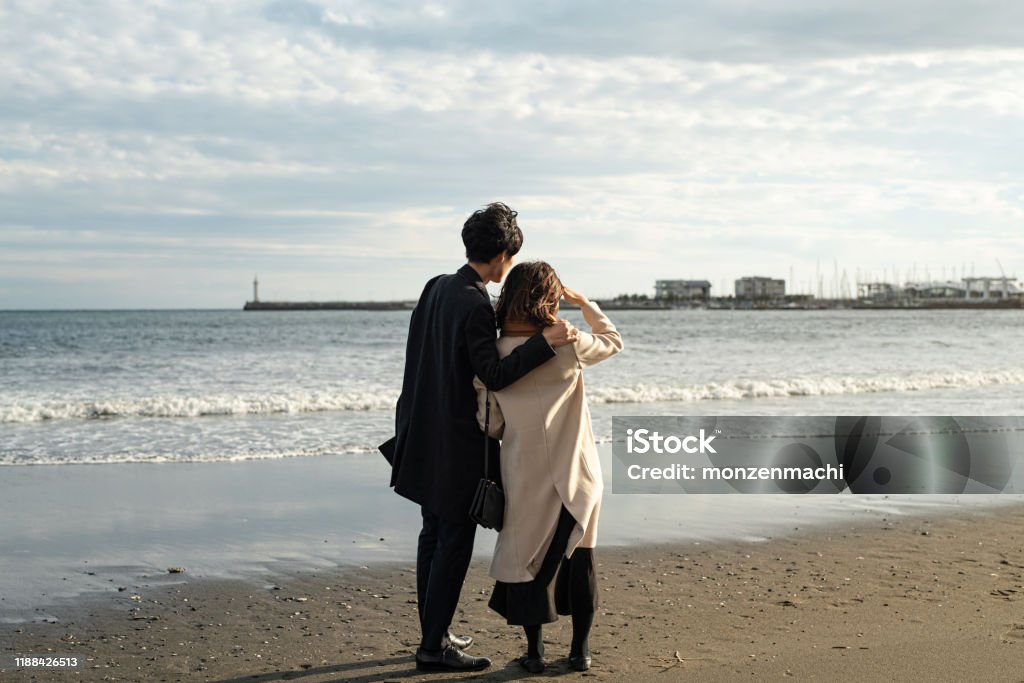 Rear view of couple standing at beach Couple dating at beach in Autumn Couple - Relationship Stock Photo