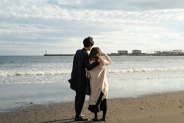 Rear view of couple standing at beach Couple dating at beach in Autumn sagami bay photos stock pictures, royalty-free photos & images