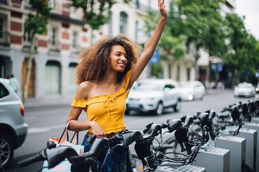 Beautiful girl taking rent-a-bike for traveling through the city and waving to someone..