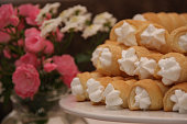 Delicious foam rolls or Schillerlocken Schaumrollen for sweet pastry arranged on white plate decorated with roses and flowers