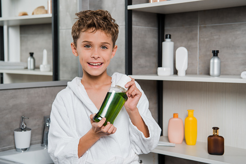 happy boy holding bottle with green mouthwash in bathroom
