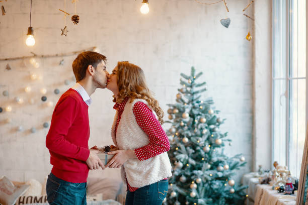 istock Young couple kissing while holding together a present box, with Christmas decorations in background 1188433256