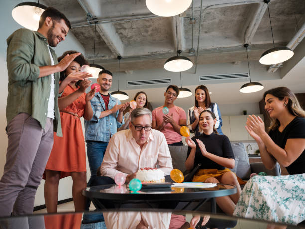 istock Mature latin man blowing birthday candles at work with colleagues 1188440055