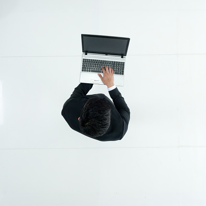 Full length / one man only / one person / directly above view / aerial view of adult handsome people black hair / short hair chinese ethnicity / east asian ethnicity male / young men businessman / business person standing in front of white background in the office wearing businesswear / a suit who is working and using laptop / computer