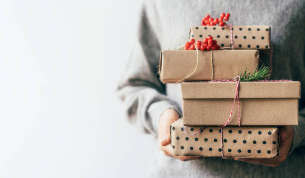 istock Elegant female hands holding gift boxes in plain brown paper decorated with red berries. 1188446478