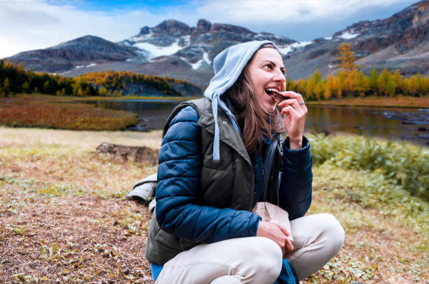 młoda kobieta turystka korzystających z przerwy na przekąskę na szlaku nad jeziorem - cookie food snack healthy eating zdjęcia i obrazy z banku zdjęć