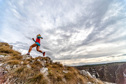 Action photo of athlete woman trail runner running and climbing over mountain cliff. Extreme terrain.