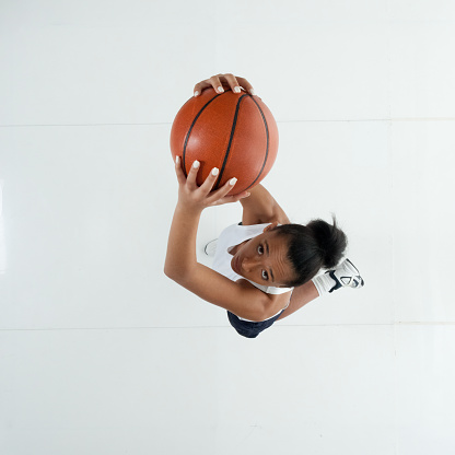 Directly above view / aerial view / full length / one person / looking at camera / looking up of 20-29 years old adult beautiful african ethnicity / african-american ethnicity female / young women basketball player / athlete / sportsperson jumping / mid-air / exercising wearing sports clothing / sports uniform who is joy / excited who is passing - sport and holding basketball - ball / using sports ball / basketball - sport / sport