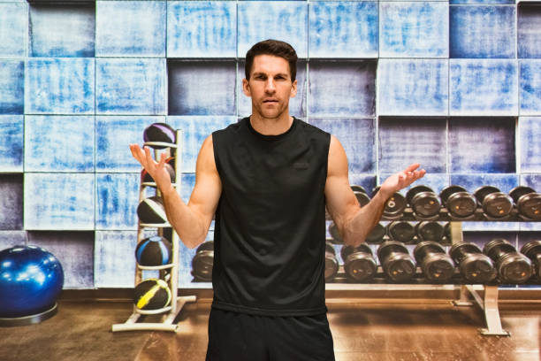 One man only / one person / waist up / front view of handsome people male / young men sleeveless / athlete / instructor exercising / standing / doing relaxation exercise at the health club in the gym and using exercise equipment / fitness ball stock photo