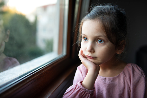 Portrait of a preschool age girl looking through window.