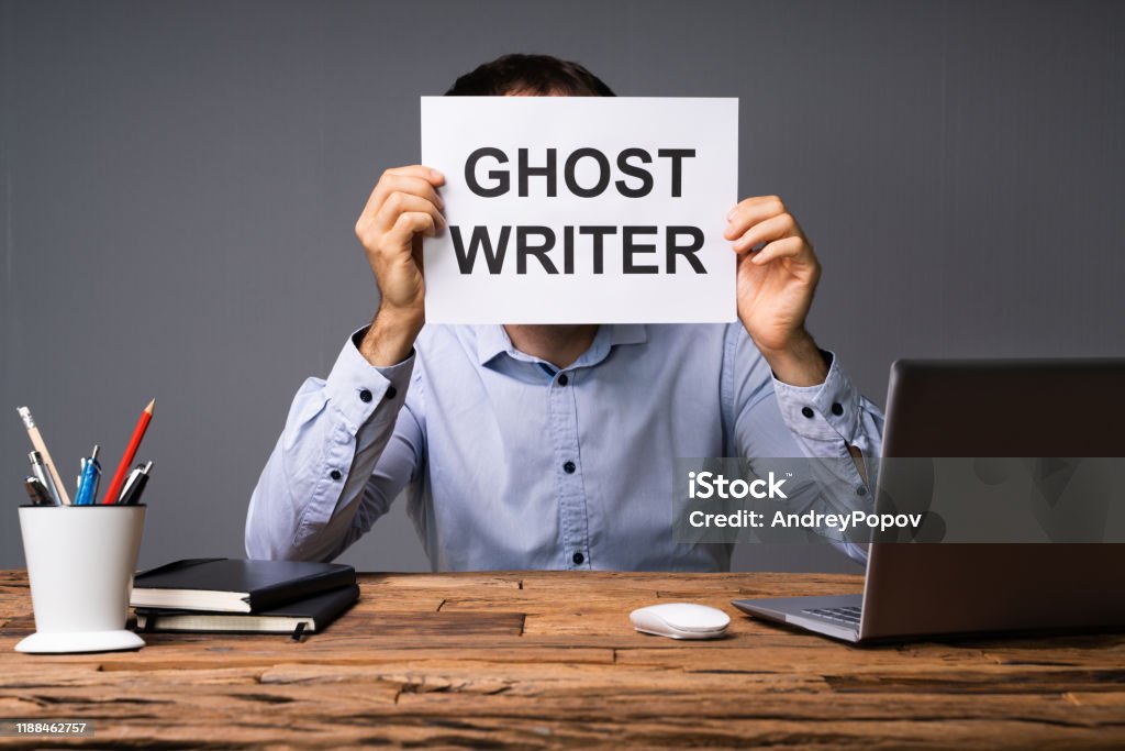 Businessman Hiding His Face Behind Card With Ghost Writer Text Businessman Hiding His Face Behind Card With Ghost Writer Text Sitting In Front Of Desk Adult Stock Photo