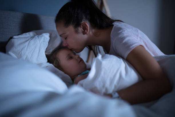 istock Mother Kissing Her Sleeping Daughter On Bed 1188464307