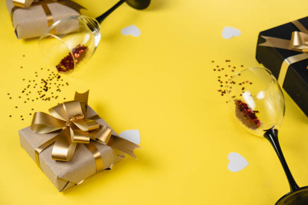 istock Holiday background. Two clinking wine glasses, various handmade gift boxes decorated with pink heart confetti on yellow background. Valentines day concept. Flat lay, top view, copy space 1188467260