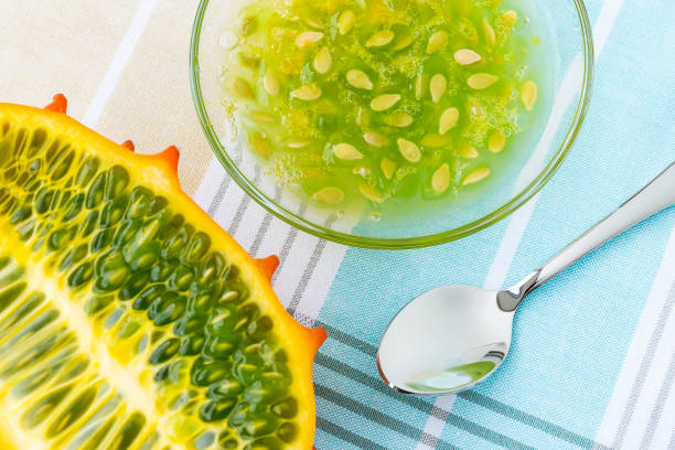 die hälfte des orangen kiwano (cucumis metuliferus, gehörnte melone), glasschüssel mit kiwano-pulp und einem löffel auf einer tischdecke. obst, gemüse, vegetarische und gesunde ernährung. - kawani fruit stock-fotos und bilder