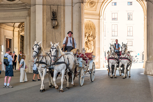 Carriages move past one of the gates at Hofburg Palace in downtown Vienna Austria on a sunny day.
