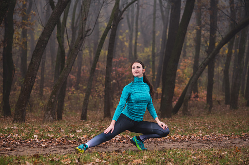 Beautiful fit girl doing workout performing lateral lunges outdoors. Fallen foliage on the ground, autumn foggy morning.