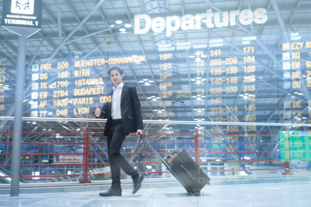 Young handsome businessman with suit walking happily through airport with rolling suitcase waiting for departure, double explosure with destination board