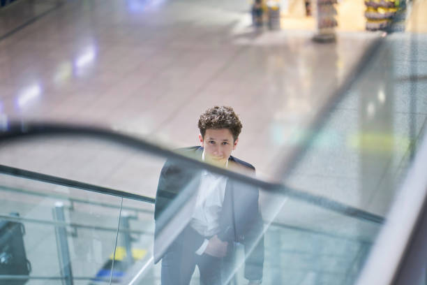 istock Young handsome smiling businessman inside the airport on an escalator with his rolling suitcase, light reflections 1188481201