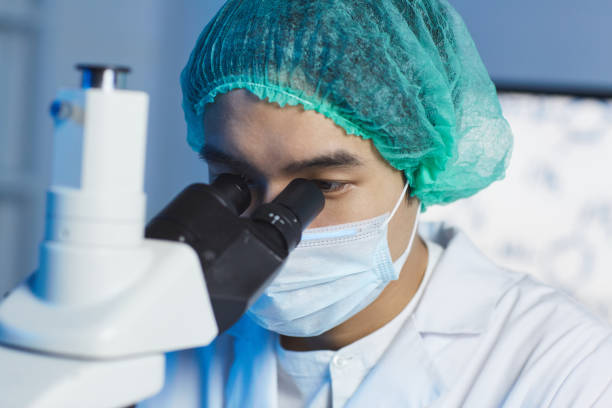 istock Close-up of young Asian clinician in sterile cap and mask working with microscope while analyzing substance 1188486389