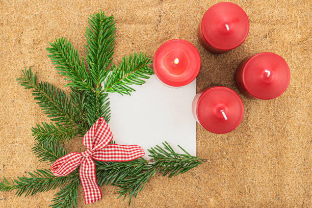 Overhead studio shot of Christmas greeting card with the four advent candles on the top right.\n\nThis is number two image out of 5: \n\n#1 - All candles are unlit \n#2 - The first advent candle is lit \n#3 - Two advent candles are lit \n#4 - Three advent candles are lit \n#5 - All advent candles are lit
