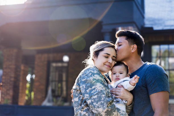 Mid adult man kisses his soldier wife While standing in their front yard, a mid adult husband kisses his soldier wife before she leaves for an assignment. The woman is holding their baby girl. war veteran stock pictures, royalty-free photos & images