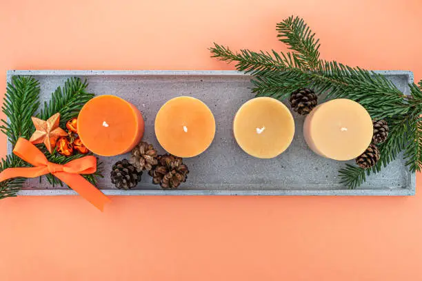 Overhead studio shot well suited for web banner of four advent candles in tones from orange to beige. The candles are on a cement tray, surrounded by pine branches, a bow, a star, pine cones and 3 bronze colored jingle bells.

This is number one image out of 5: 

#1 - All candles are unlit 
#2 - The first advent candle is lit 
#3 - Two advent candles are lit 
#4 - Three advent candles are lit 
#5 - All advent candles are lit

Color pale based on Living Coral Pantone color, the year color for 2019