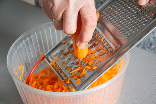 Hand of a woman grating carrot with a grater