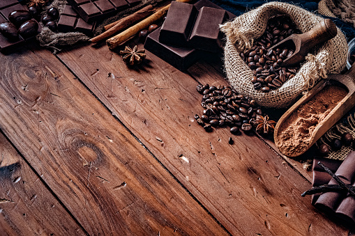 Assorted chocolate and roasted coffee beans in old fashioned style placed on top of a wooden table in rustic kitchen with copy space in frame