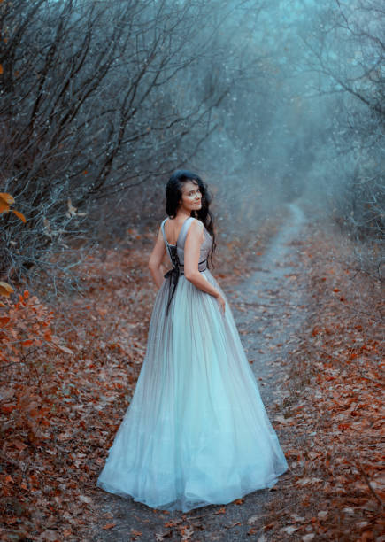 istock Attractive mystery lady in forest walks along path enjoying nature. First snow is falling. Meeting of autumn and winter. Foggy day frost on tree branches orange leaves on ground. Blue lush long dress 1188493700