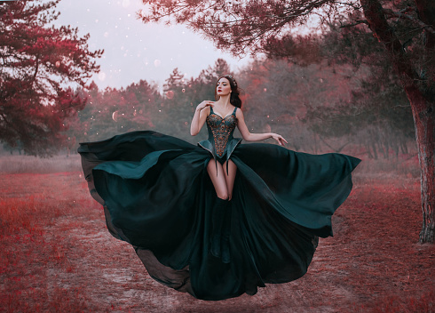 Belleza reina oscura en negro fantasía vestido creativo levita en el aire. Diseño de corsé guerrero sexy, piernas largas desnudas. Telón de fondo árboles rojos del bosque de otoño. falda de tela agitando revoloteando en el viento. Estilo de moda photo