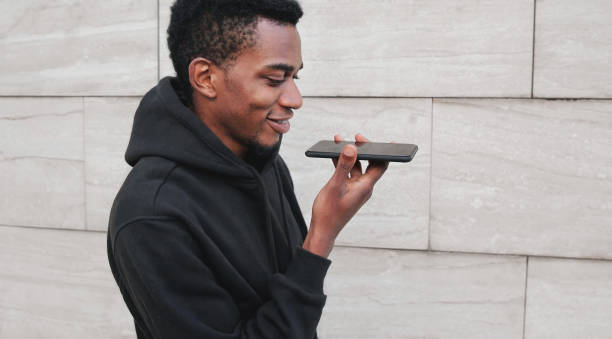 istock Portrait modern african man holding in hands smartphone using voice command recorder, assistant or takes calling, looking at phone on city street on gray wall background 1188502359