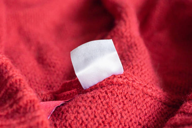 blank white laundry care clothing label on red knitted texture background - label textile shirt stitch - fotografias e filmes do acervo