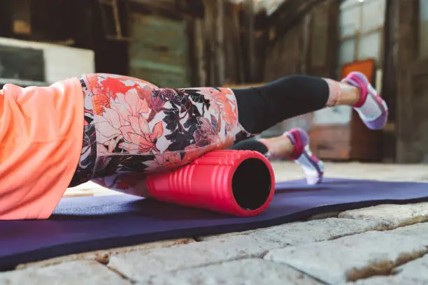 Fitness woman working out in a functional gym, using a foam roller to relax and stretch her muscles. Attractive female athlete training. Young adult woman doing workout.