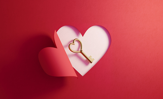 Heart shaped golden key is inside of a red folding heart shape on white background. Horizontal composition with  copy space.