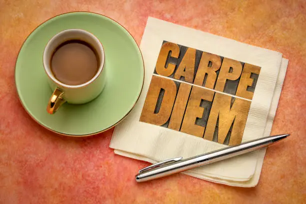 Carpe Diem  - enjoy life before it is too late, existential cautionary Latin phrase by Horace -  text in vintage letterpress wood type printing blocks on a napkin  with a cup of coffee