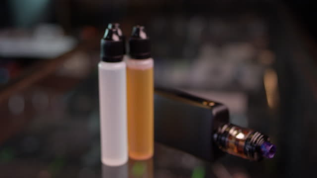 Focus on a smoking vape and vape juice on a glass counter in a smoke shop
