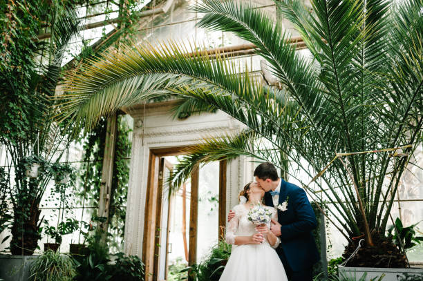 gli sposi sono in piedi e si baciano nel giardino verde botanico pieno di verde. nozze. - wedding venue foto e immagini stock