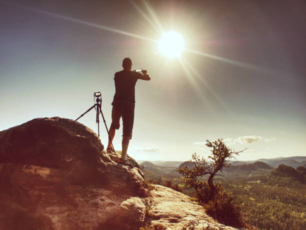 istock Traveler using smartphone, stay at tripod with camera on peak 1188555525
