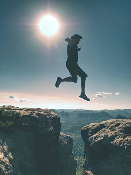 istock Jumping against Sun. Jumps over cliff. Man on trail through rocks/J 1188555566