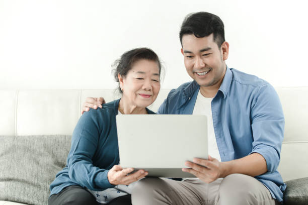 asian man teaching his mother using laptop at home, technology concept. - aging process middle women men imagens e fotografias de stock