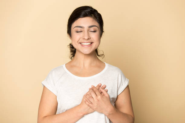благодарный счастливый красивая индийская девушка, держась за руки на груди - human face close up horizontal ideas стоковые фото и изображения