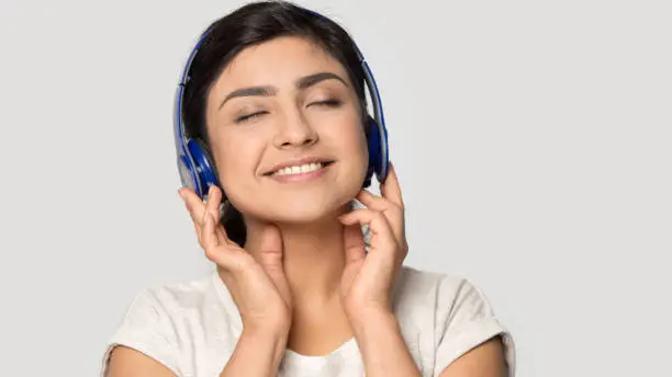 Photo of Smiling satisfied Indian girl in headphones enjoying favorite music